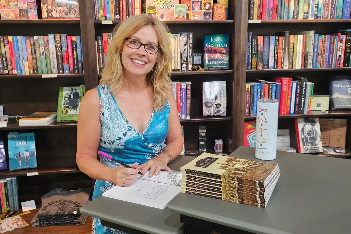 A woman in glasses signing books at a table.