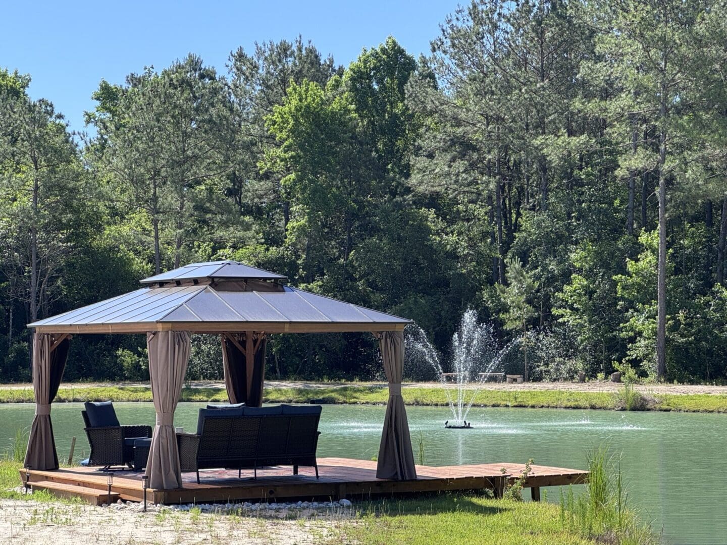 Gazebo by pond with fountain and trees.