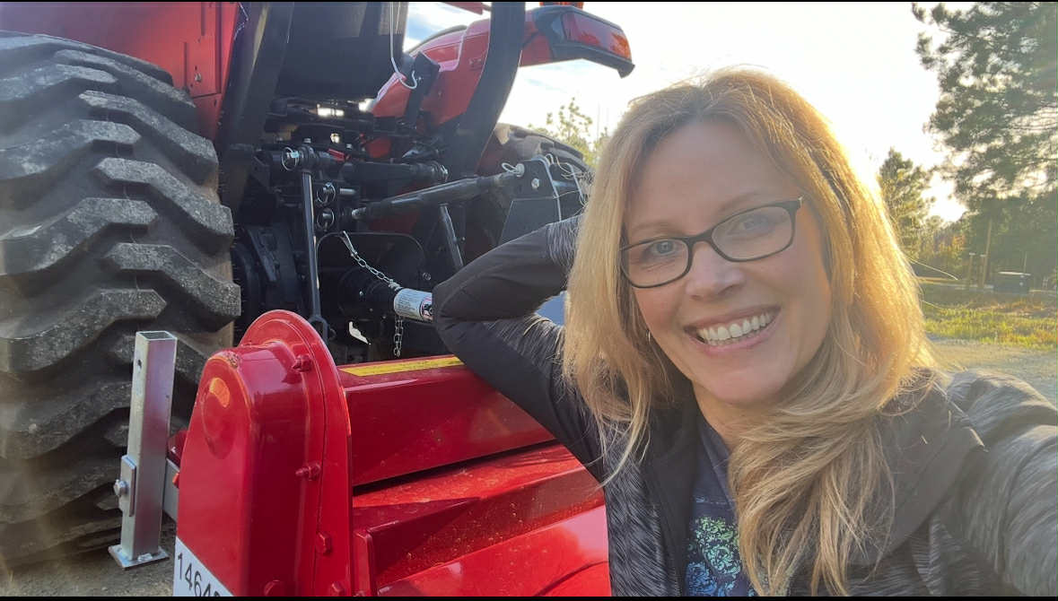 Smiling woman posing with red tractor outdoors.